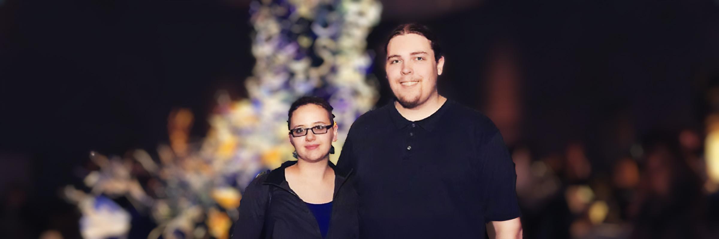 Image of a couple standing outdoors with a blurred background of celebration lights at night. 