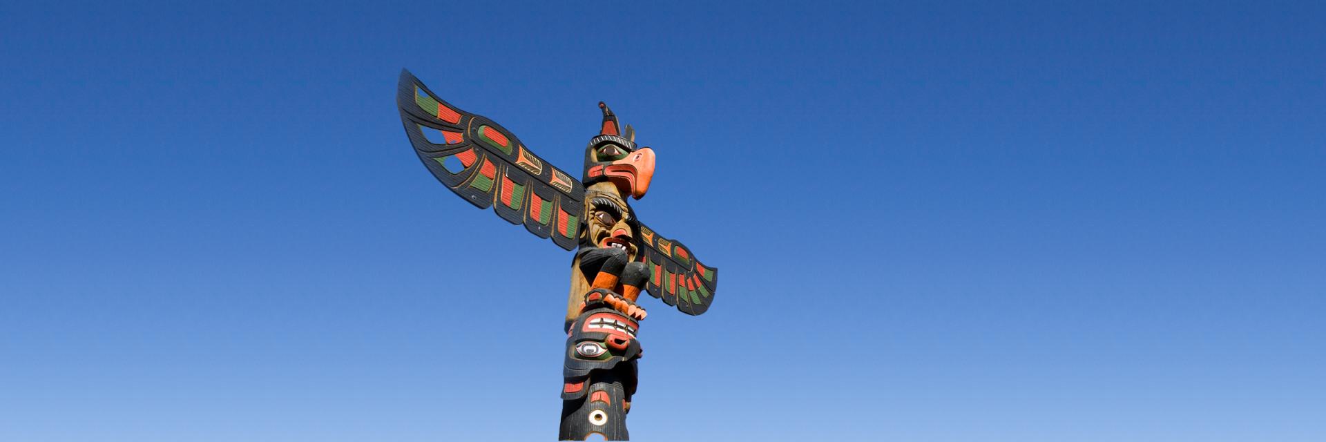 A beautiful Pacific Northwest tribal totem pole with expanded wings in front of a clear, blue sky.