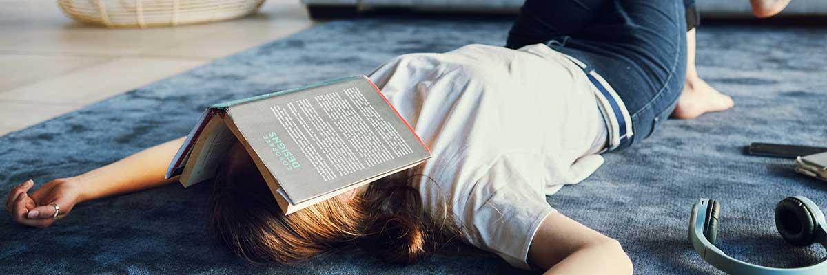 Woman lying on floor with a book over her face. 