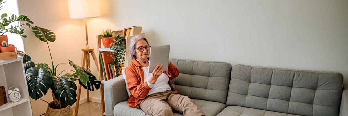 Older woman sitting on couch looking at iPad.