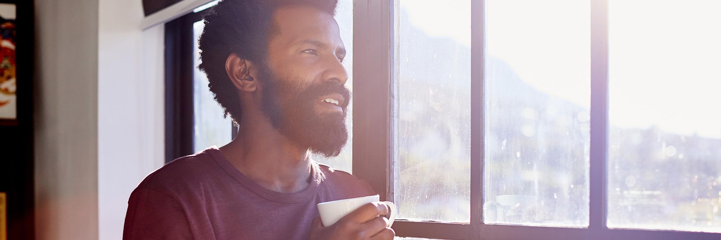 Young man drinking coffee, looking thoughtfully out a window