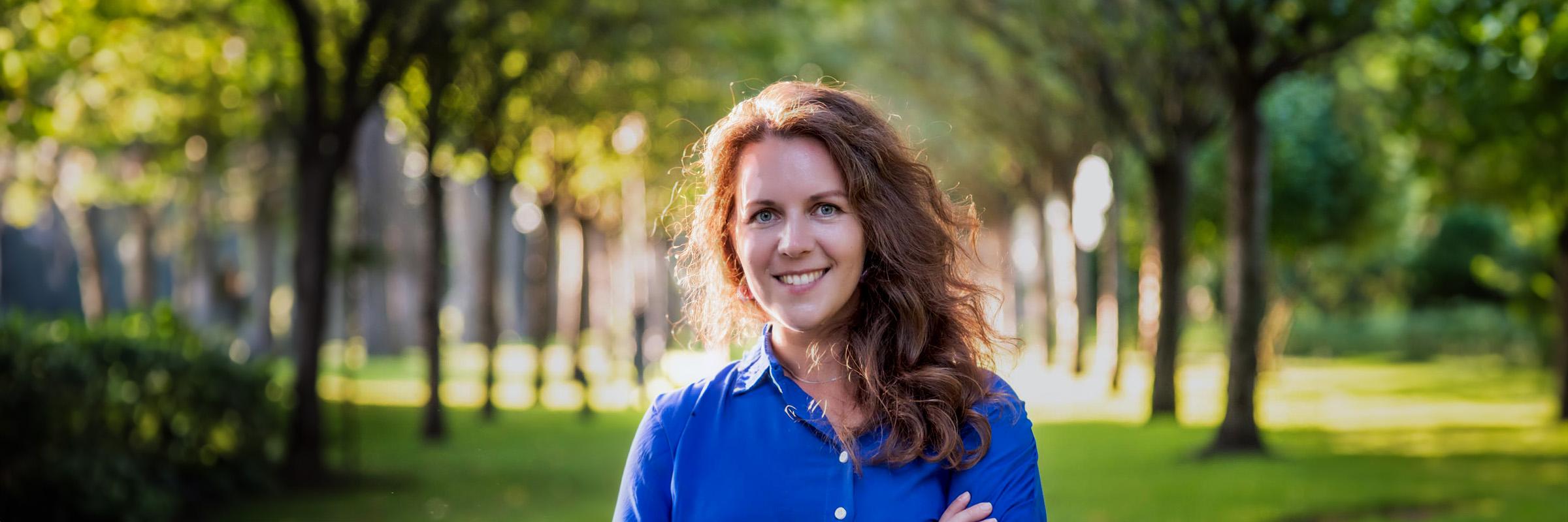 Photo of a female smiling in outdoors with two rows of trees aligned behind her.