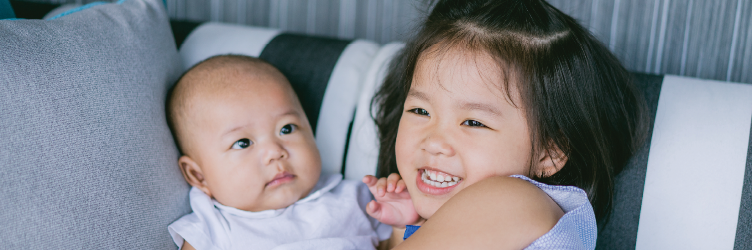 A photo of a newborn and young child smiling on the couch.