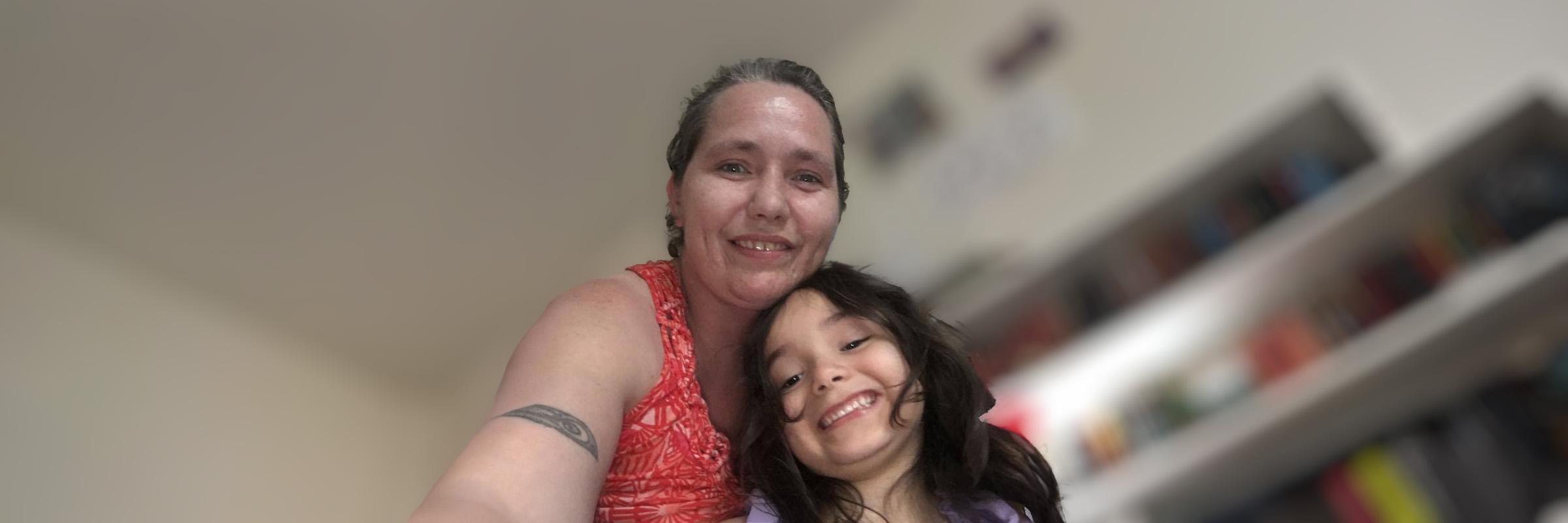 A photo of a mother and her child daughter with blurred indoor background behind them. 