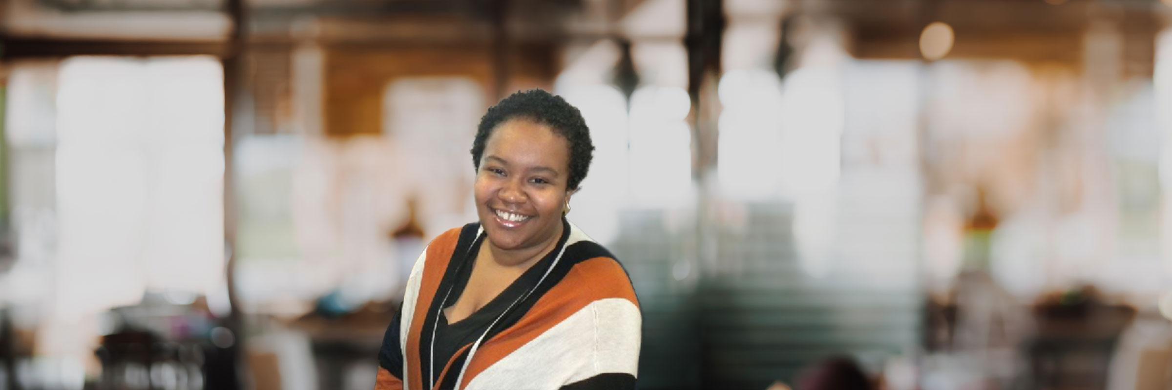 Miranda Boyd in a black, orange, and white sweater, in an office, smiling at the camera